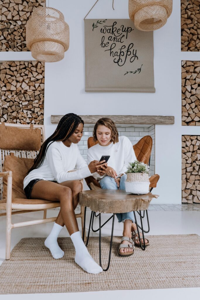 Two women sitting in a cozy Scandinavian-style interior enjoying a conversation over a smartphone.